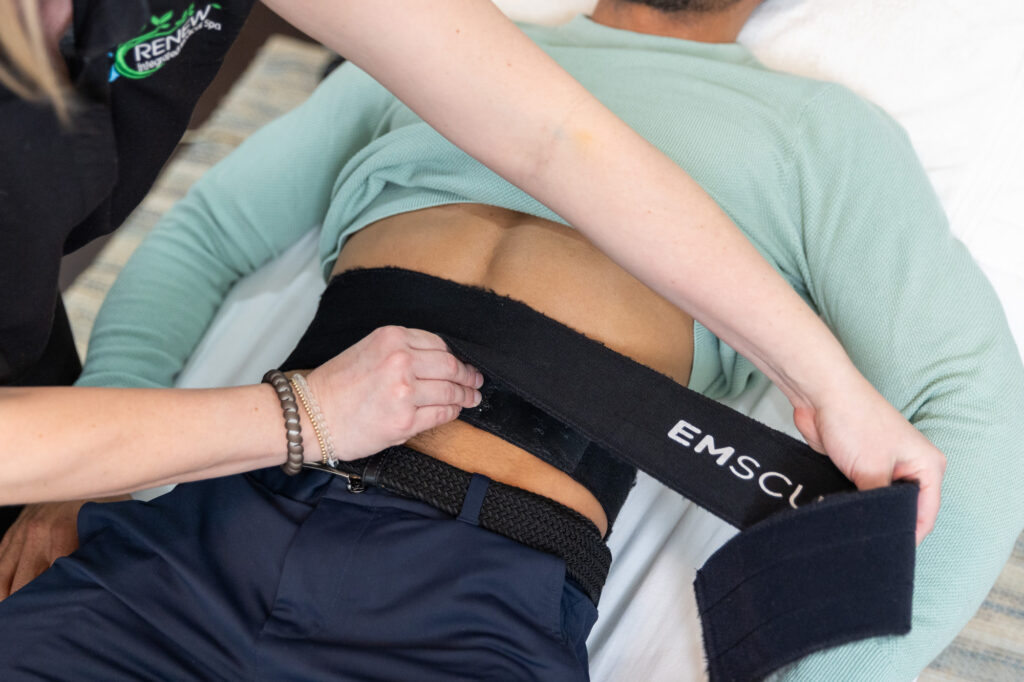 A close up image of a provider at Spa 29 getting a male patient ready to undergo a sessions of Emsculpt NEO near St. Simons Island, GA by strapping the device paddles to his abdomen.